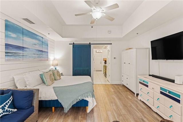 150 Salt Air Dr Unit 219, Saint Simons Island, GA 31522 - bedroom featuring a barn door, a tray ceiling, light wood-type flooring, and ceiling fan