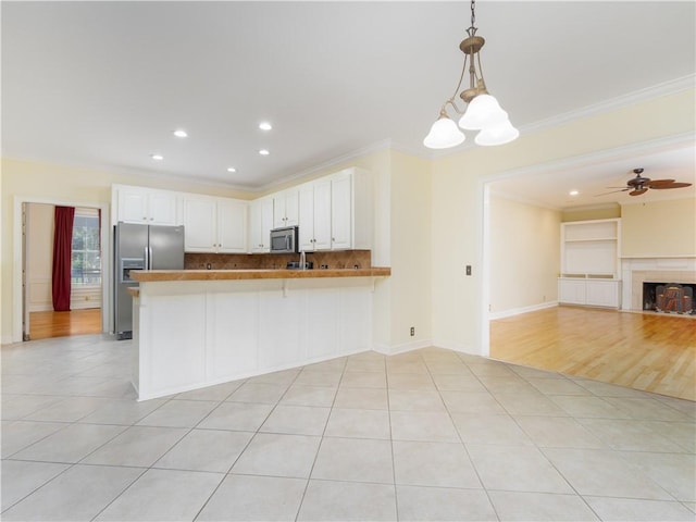 kitchen featuring crown molding, kitchen peninsula, hanging light fixtures, appliances with stainless steel finishes, and white cabinetry