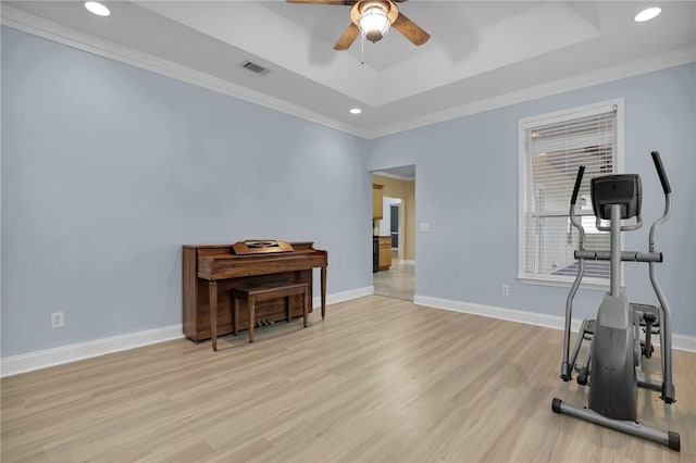 exercise room featuring ornamental molding, light hardwood / wood-style floors, a raised ceiling, and ceiling fan