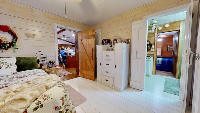 bedroom with lofted ceiling, light hardwood / wood-style flooring, a textured ceiling, and wood walls