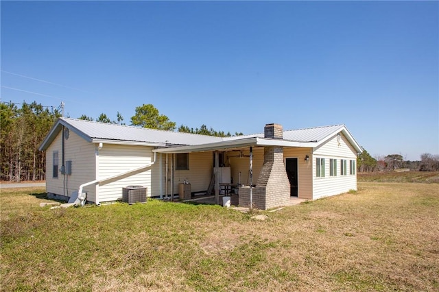 rear view of house featuring a yard, central air condition unit, and metal roof