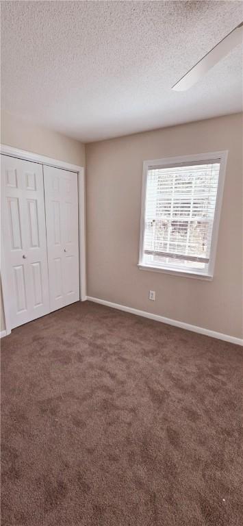 unfurnished bedroom featuring dark carpet, a closet, and a textured ceiling