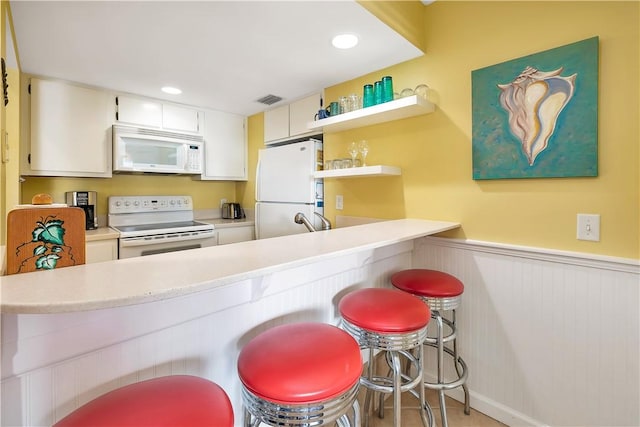 kitchen with white cabinets, white appliances, kitchen peninsula, and a breakfast bar area