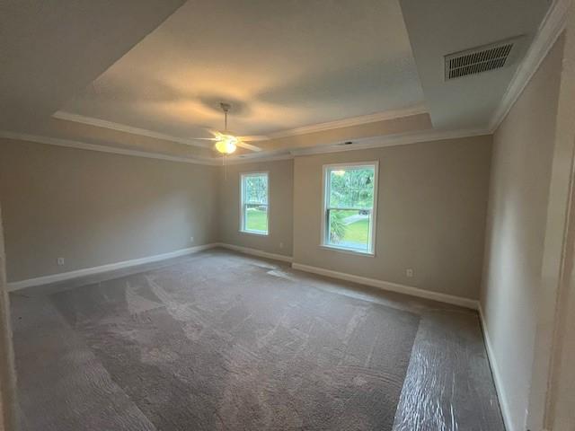 unfurnished room with a tray ceiling, crown molding, ceiling fan, and dark colored carpet