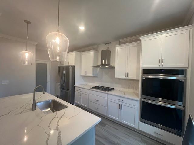 kitchen with sink, stainless steel appliances, hanging light fixtures, wall chimney range hood, and white cabinets