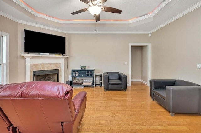 living area featuring ornamental molding, a fireplace, light wood-style flooring, a tray ceiling, and ceiling fan