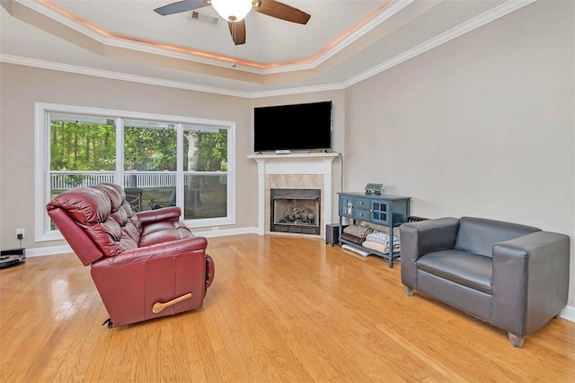 living area with a tray ceiling, crown molding, a ceiling fan, and wood finished floors