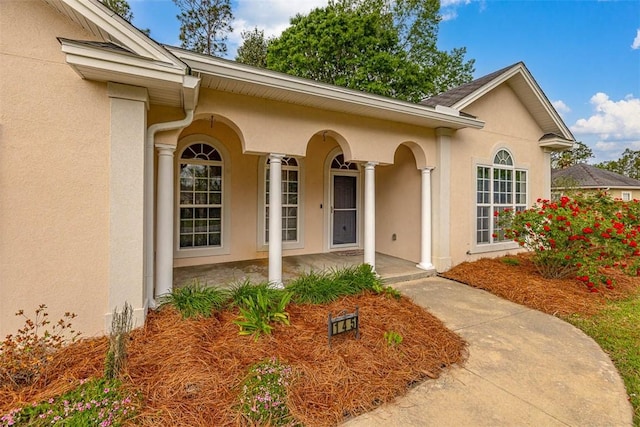 doorway to property with a porch and stucco siding