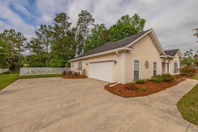 view of side of home featuring a garage, stucco siding, fence, and concrete driveway
