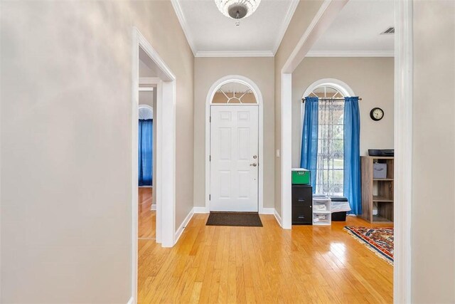 foyer featuring light wood-type flooring, baseboards, ornamental molding, and visible vents