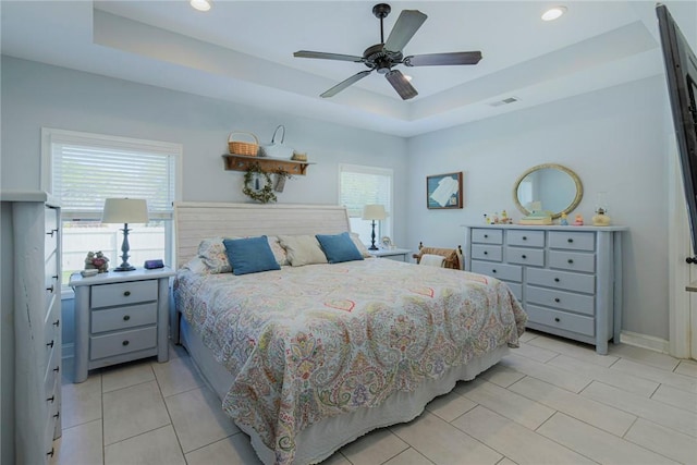 bedroom with a tray ceiling, multiple windows, and visible vents