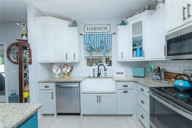 kitchen featuring a sink, white cabinetry, appliances with stainless steel finishes, light stone countertops, and glass insert cabinets