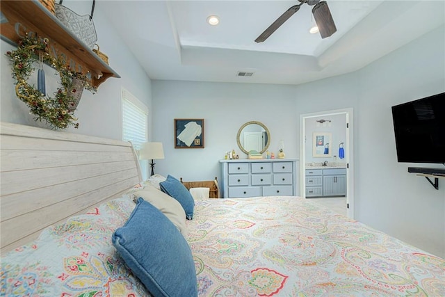 bedroom with a ceiling fan, a tray ceiling, visible vents, and connected bathroom