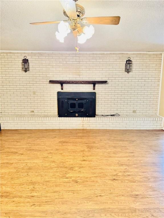 unfurnished living room featuring brick wall, wood-type flooring, a wood stove, ceiling fan, and a textured ceiling