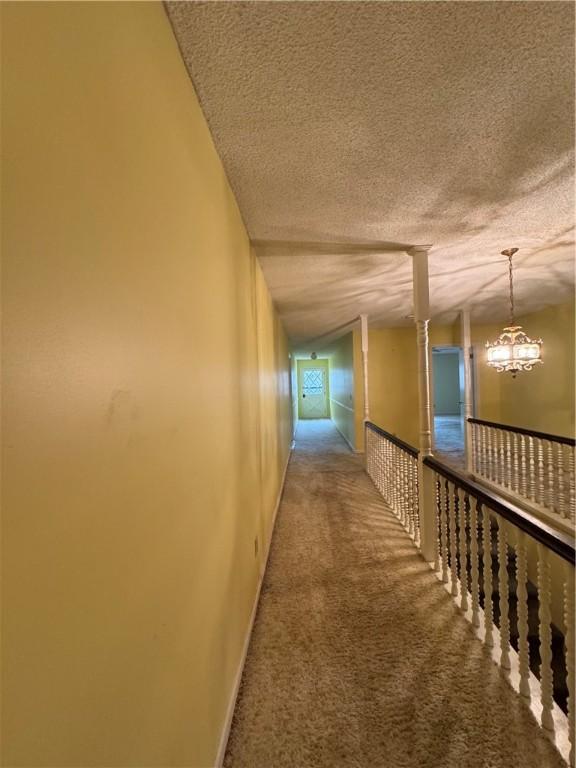 corridor featuring a notable chandelier, lofted ceiling, carpet, and a textured ceiling
