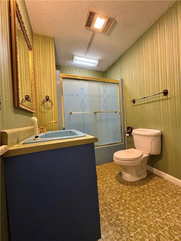 full bathroom featuring shower / bath combination with glass door, vanity, toilet, and a textured ceiling