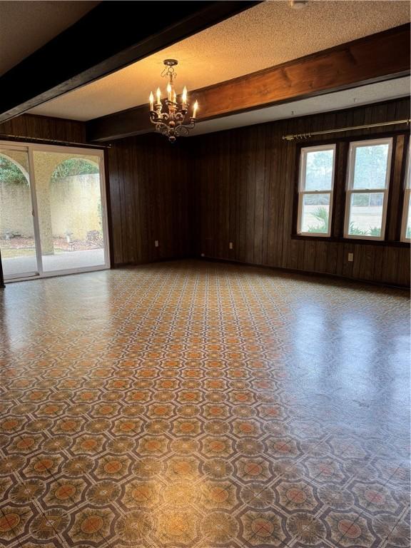 spare room with beam ceiling, wooden walls, a textured ceiling, and a chandelier