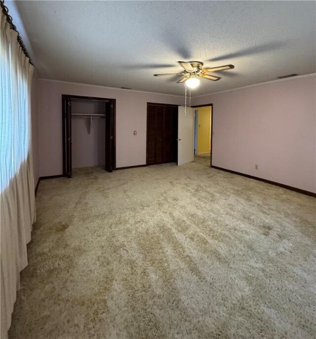 unfurnished bedroom featuring light carpet, ceiling fan, two closets, and a textured ceiling