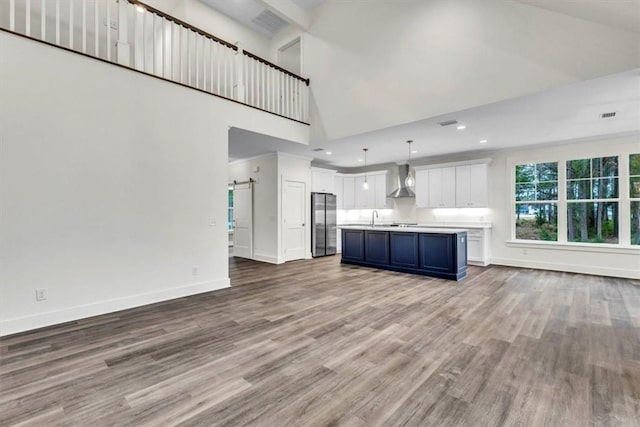 unfurnished living room with a towering ceiling, wood-type flooring, a barn door, and sink