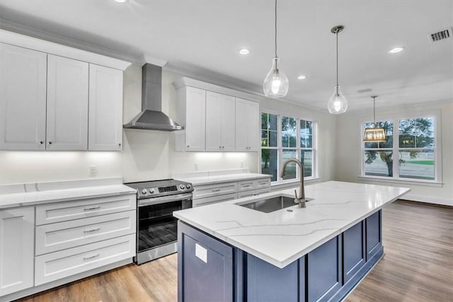 kitchen with electric stove, wall chimney range hood, sink, white cabinetry, and a center island with sink