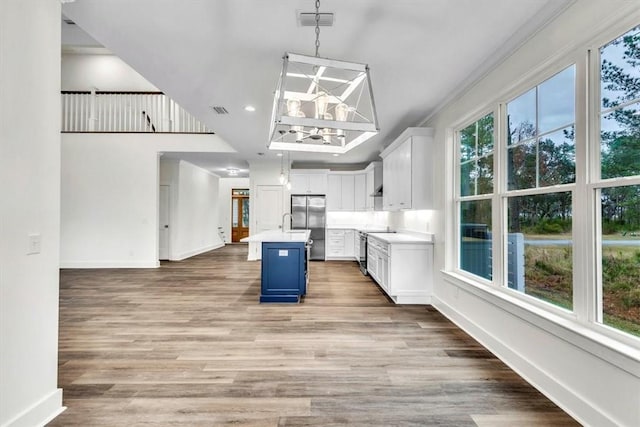 kitchen featuring a breakfast bar area, appliances with stainless steel finishes, a kitchen island with sink, white cabinetry, and decorative light fixtures