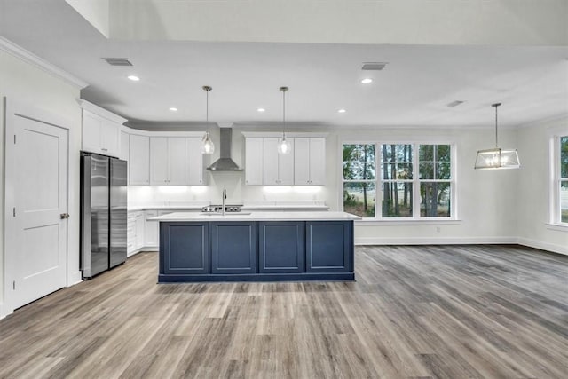 kitchen with pendant lighting, white cabinets, stainless steel refrigerator, and wall chimney exhaust hood