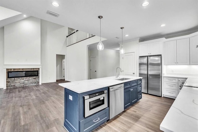 kitchen with sink, stainless steel appliances, blue cabinets, white cabinets, and a center island with sink