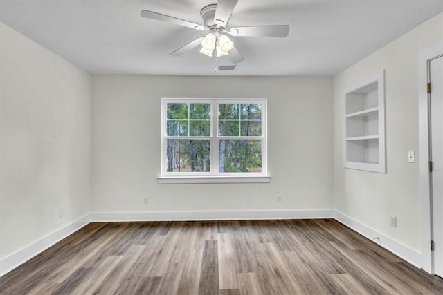 empty room featuring built in shelves, ceiling fan, and wood-type flooring