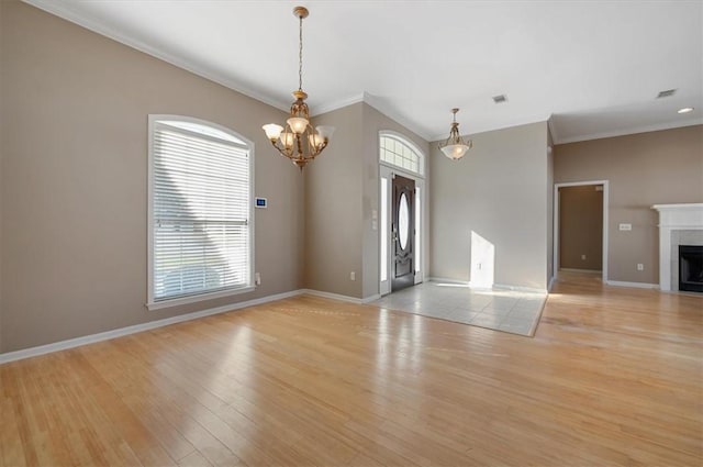 unfurnished living room featuring a fireplace, a notable chandelier, ornamental molding, and light hardwood / wood-style flooring