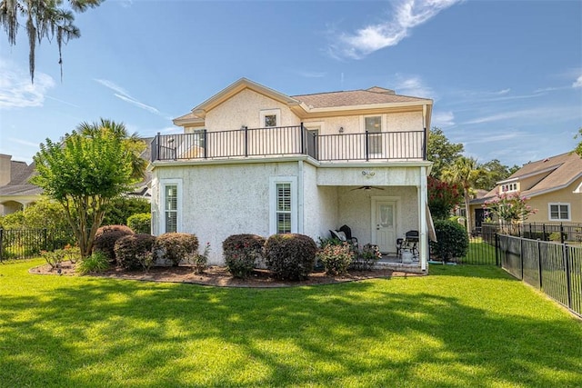 rear view of house featuring ceiling fan, a balcony, and a yard