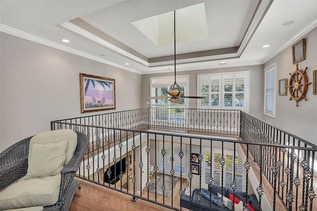 corridor with a raised ceiling, hardwood / wood-style flooring, a textured ceiling, and ornamental molding