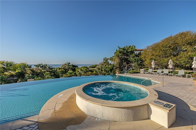 view of pool featuring a water view, a patio, and a hot tub