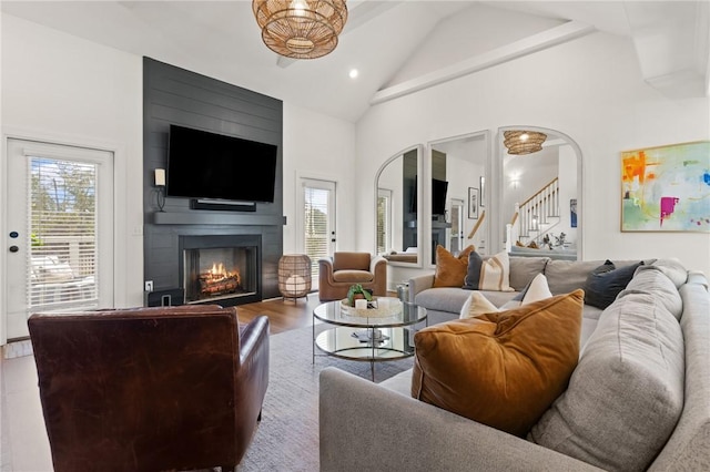 living area with arched walkways, high vaulted ceiling, a fireplace, wood finished floors, and stairway