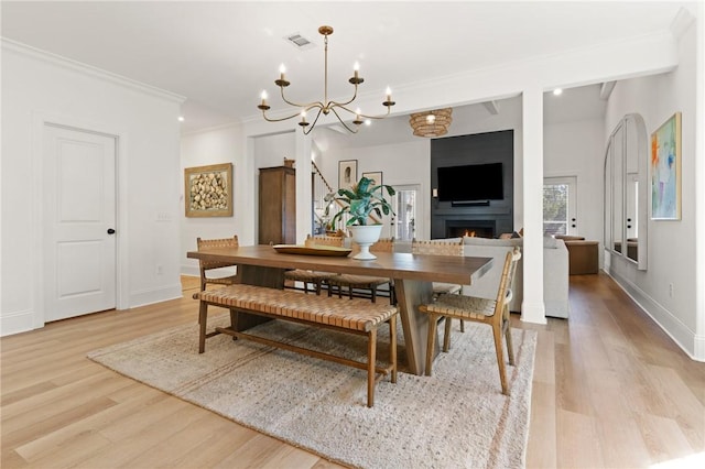 dining area featuring visible vents, light wood-style flooring, ornamental molding, a warm lit fireplace, and baseboards