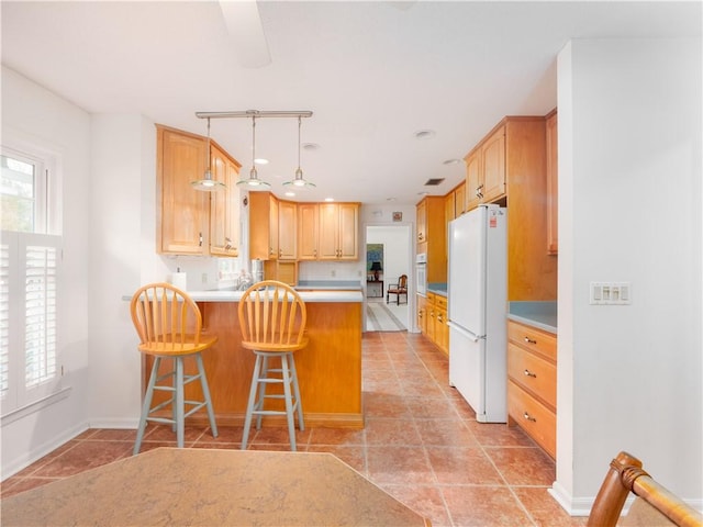 kitchen featuring white appliances, a kitchen breakfast bar, light brown cabinetry, decorative light fixtures, and kitchen peninsula