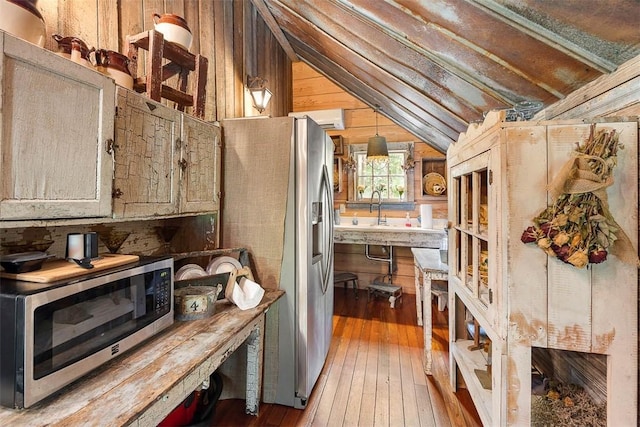 kitchen featuring lofted ceiling, appliances with stainless steel finishes, wood finished floors, decorative light fixtures, and light countertops