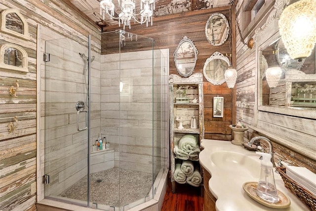 bathroom featuring an inviting chandelier, a shower stall, a sink, and wood walls