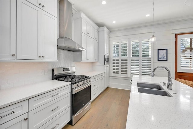 kitchen with wall chimney exhaust hood, stainless steel appliances, sink, white cabinetry, and hanging light fixtures