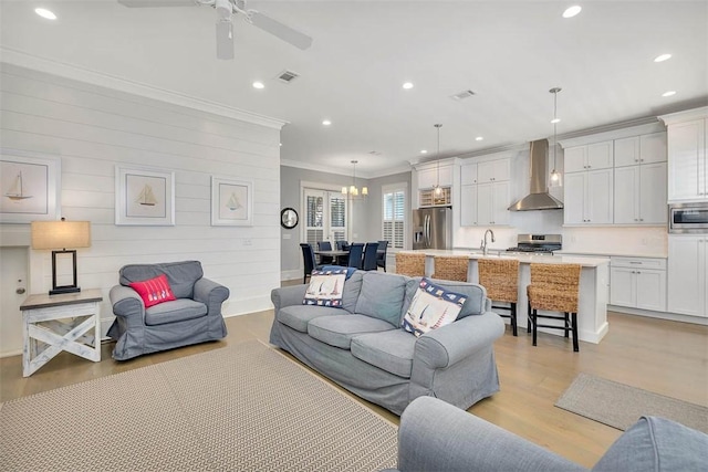 living room featuring sink, crown molding, wooden walls, ceiling fan with notable chandelier, and light wood-type flooring