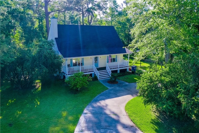 view of front facade featuring a front lawn, covered porch, a chimney, and concrete driveway