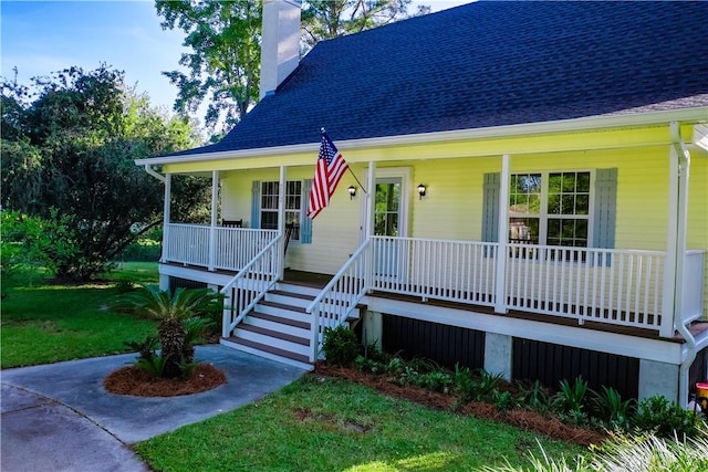 view of front of home with a porch, roof with shingles, a front yard, and a chimney