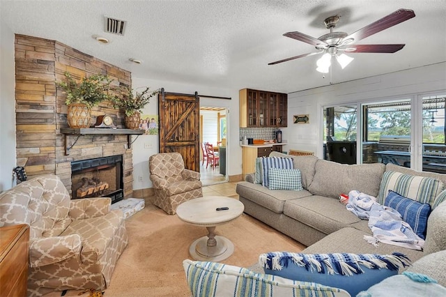 tiled living room with a textured ceiling, ceiling fan, wooden walls, a barn door, and a stone fireplace