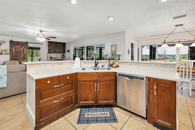 kitchen featuring sink, stainless steel dishwasher, a barn door, light tile patterned floors, and a textured ceiling