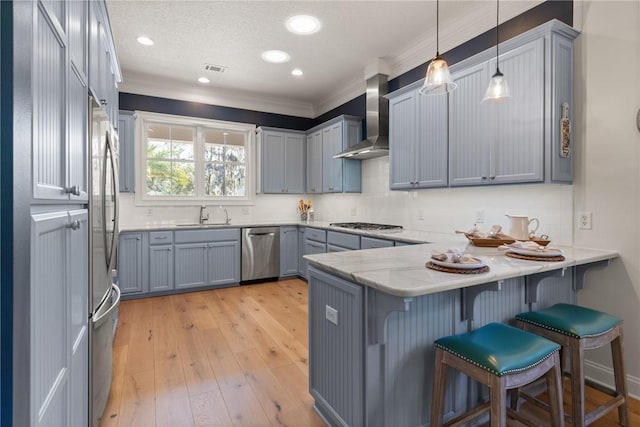 kitchen with stainless steel appliances, kitchen peninsula, hanging light fixtures, and wall chimney range hood