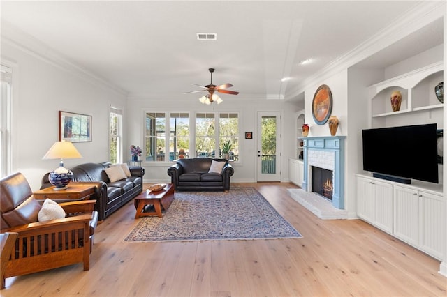 living room featuring crown molding, a brick fireplace, built in features, and light wood-type flooring