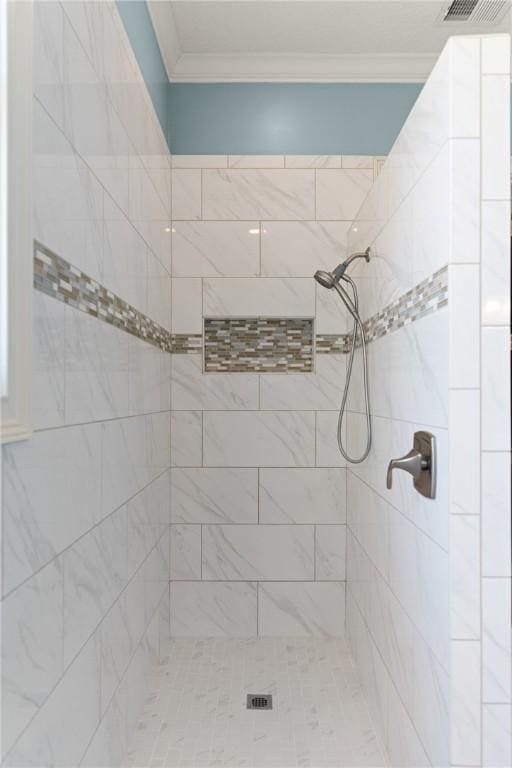 bathroom with ornamental molding and a tile shower