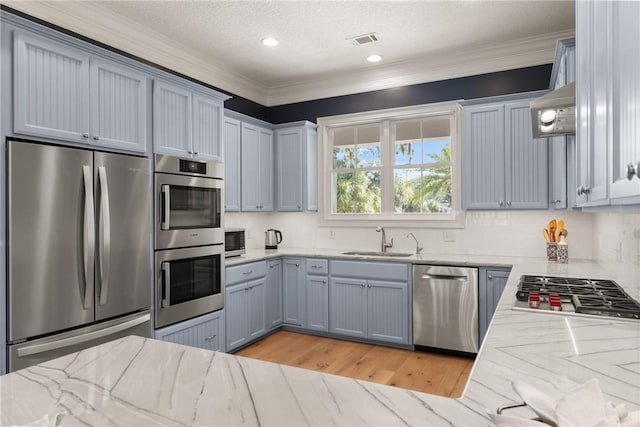 kitchen featuring sink, ornamental molding, appliances with stainless steel finishes, light hardwood / wood-style floors, and decorative backsplash