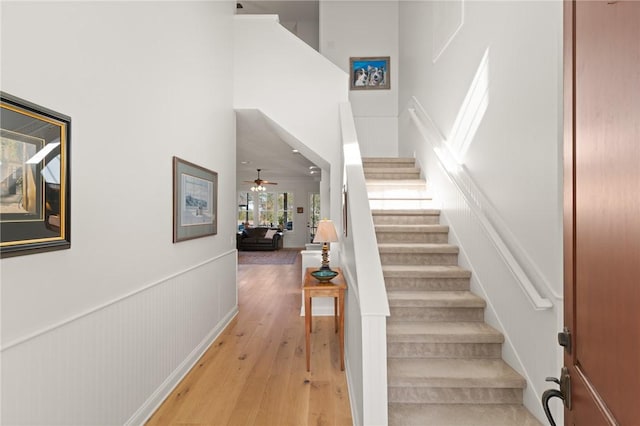 stairs with hardwood / wood-style floors, ceiling fan, and a high ceiling