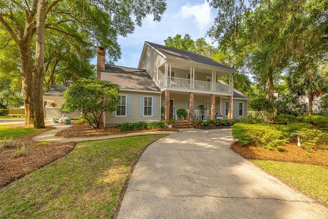 view of front of property with a porch, a chimney, a balcony, and concrete driveway