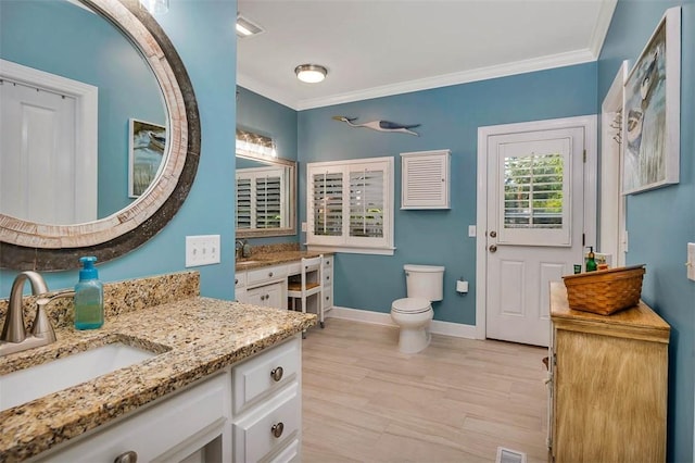 bathroom featuring crown molding, two vanities, baseboards, toilet, and wood finished floors